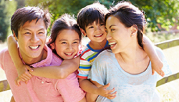 A happy family with two children enjoying a sunny day outdoors, smiling and hugging each other near a wooden fence.