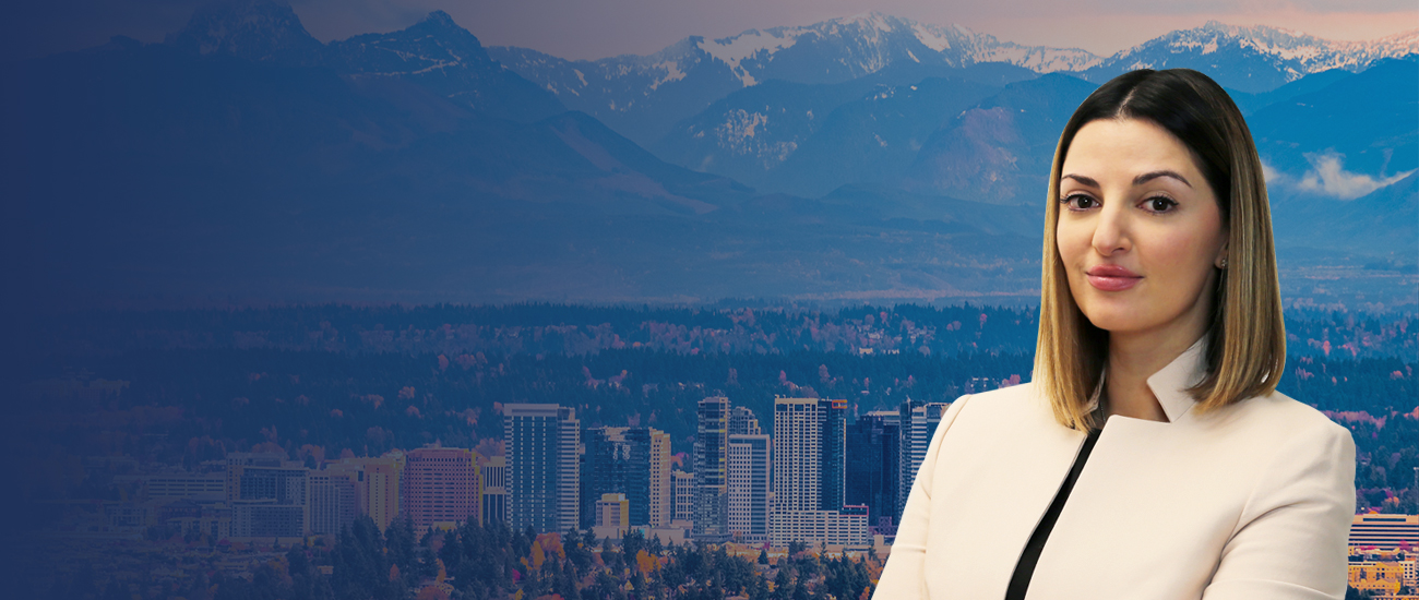 Alice Bagirova in a white blazer stands in front of a cityscape with autumn-colored trees and mountainous backdrop.