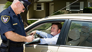 A police officer writing a ticket to a driver during a traffic stop outside a residential area.
