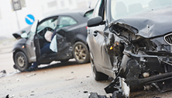 Two cars after a collision on a road with deployed airbags and significant front-end damage to both vehicles.